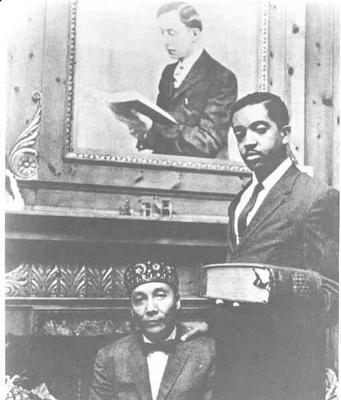 Elijah Muhammad and his son W. D. Mohammed  (also known as Wallace Muhammad) pose in front of a portrait of W. D. Fard (also known as W. F. Muhammad)