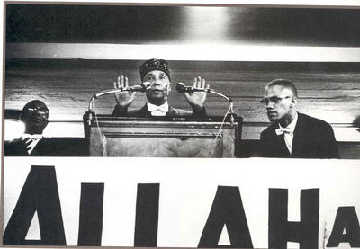 Elijah Muhammad speaking at rally with Malcolm X looking on